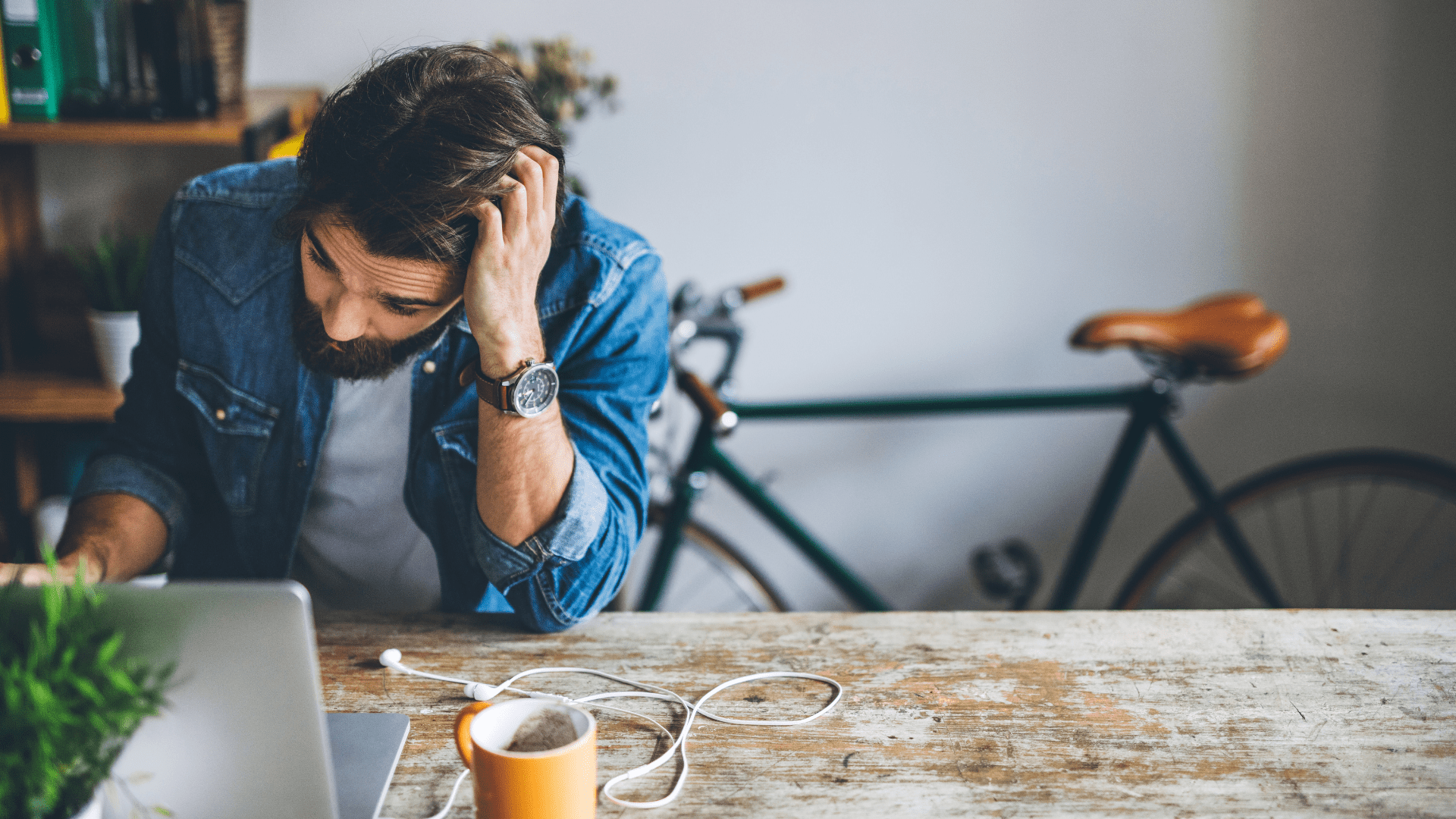 Bearded freelancer at desk with a cup of tea, stressed while preparing business registration paperwork.